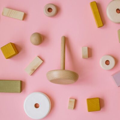 A variety of wooden Montessori toys arranged on a pink background in a flat lay style.