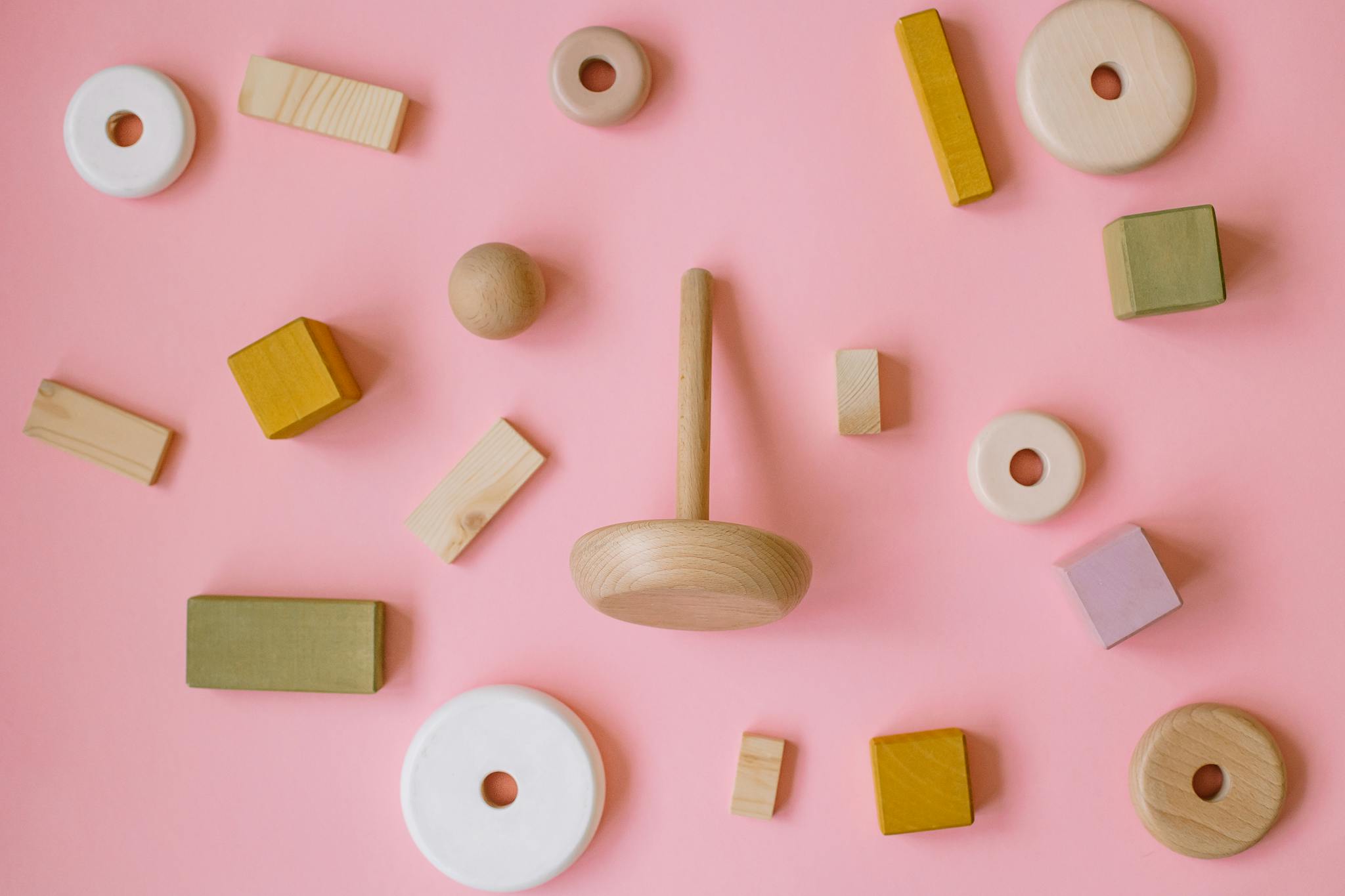 A variety of wooden Montessori toys arranged on a pink background in a flat lay style.
